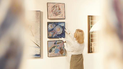 Lady adjusting paintings with gloves on